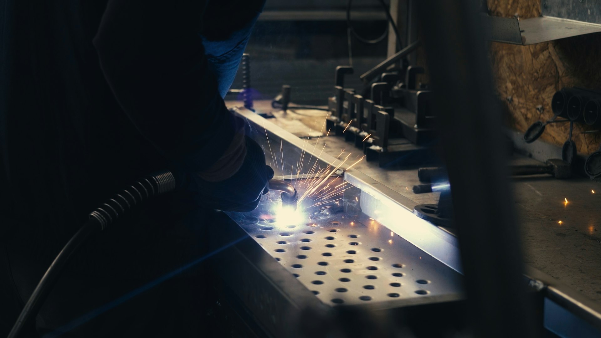 A fabricator welding a perforated steel component in a workshop, sparks flying, representing Superior Engineering's in-house build quality.